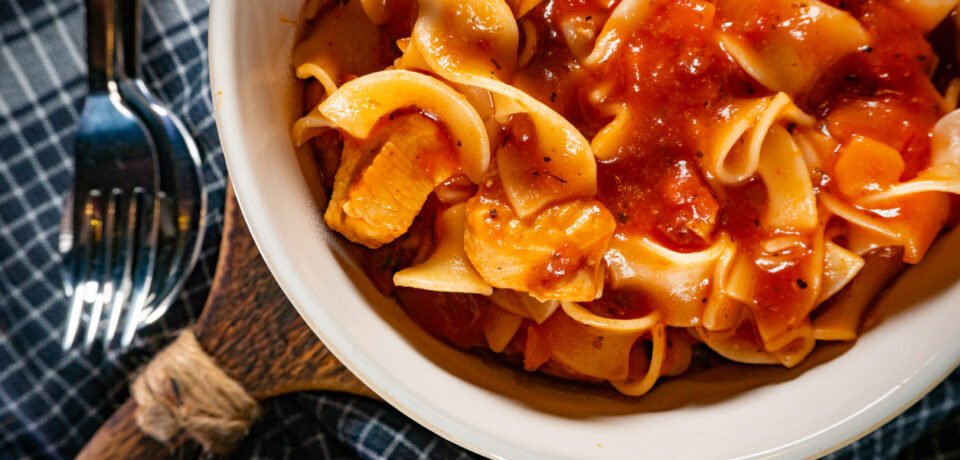 Pieces of chicken with noodle in tomato and herb sauce. Shallow depth of field.
